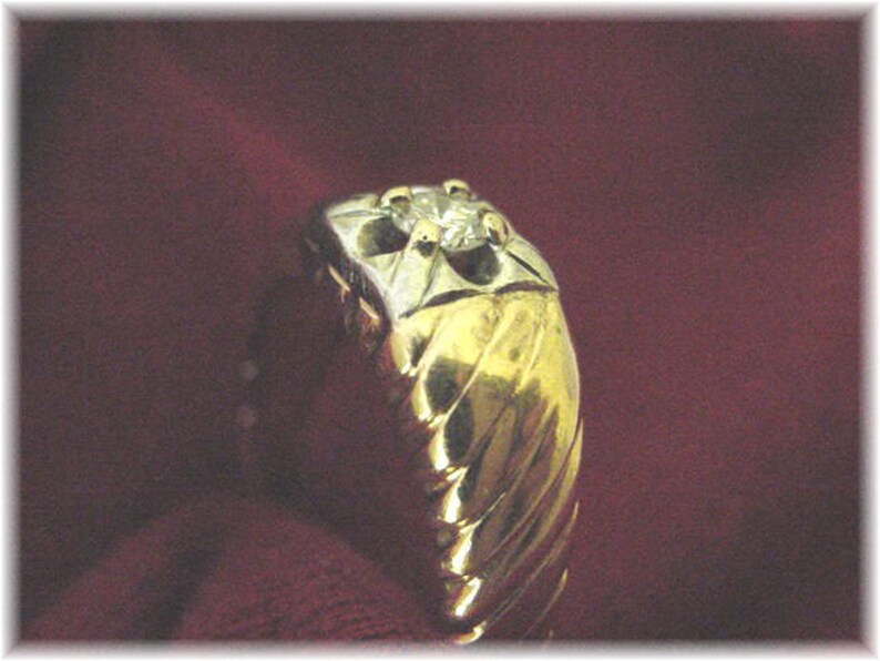May include: A gold ring with a single diamond set in the center. The ring has a textured, twisted band.