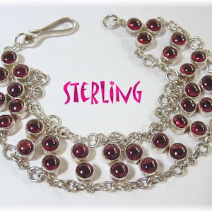 May include: A sterling silver bracelet with multiple rows of round, deep red gemstones. The bracelet has a delicate chain design and a secure clasp. The word "STERLING" is displayed in pink text.