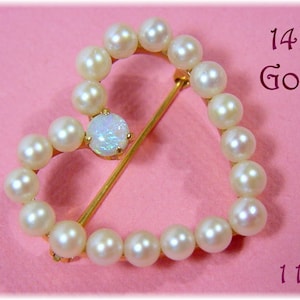 May include: A heart-shaped brooch made of 14K gold, adorned with creamy pearls and a central opal. The brooch is 1 1/8 inches in diameter. The text "14K Gold" is visible.