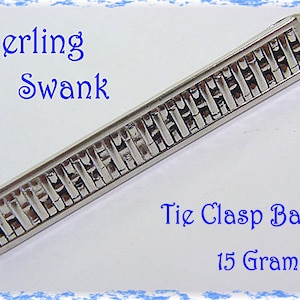 May include: A silver-colored tie clasp bar with a woven design. The text "Sterling Swank" is above the bar, and "Tie Clasp Bar" and "15 Grams" are below. The clasp is a rectangular shape.