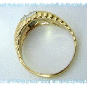 May include: A gold ring with a single, clear gemstone set in the center. The ring has a textured band.