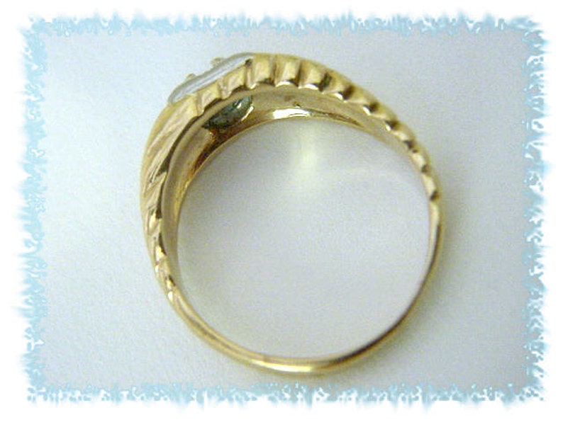 May include: A gold ring with a single, clear gemstone set in the center. The ring has a textured band.