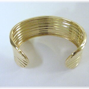 May include: A gold bangle bracelet with a ridged design. The bracelet is open and has a simple, elegant style.