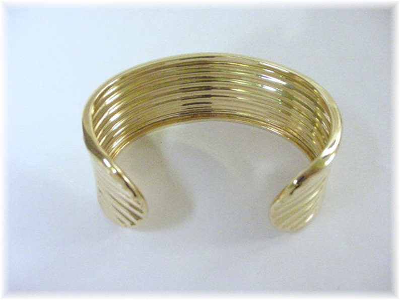 May include: A gold bangle bracelet with a ridged design. The bracelet is open and has a simple, elegant style.