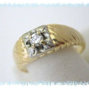 May include: A gold and white ring with a single diamond in the center. The ring has a textured band.