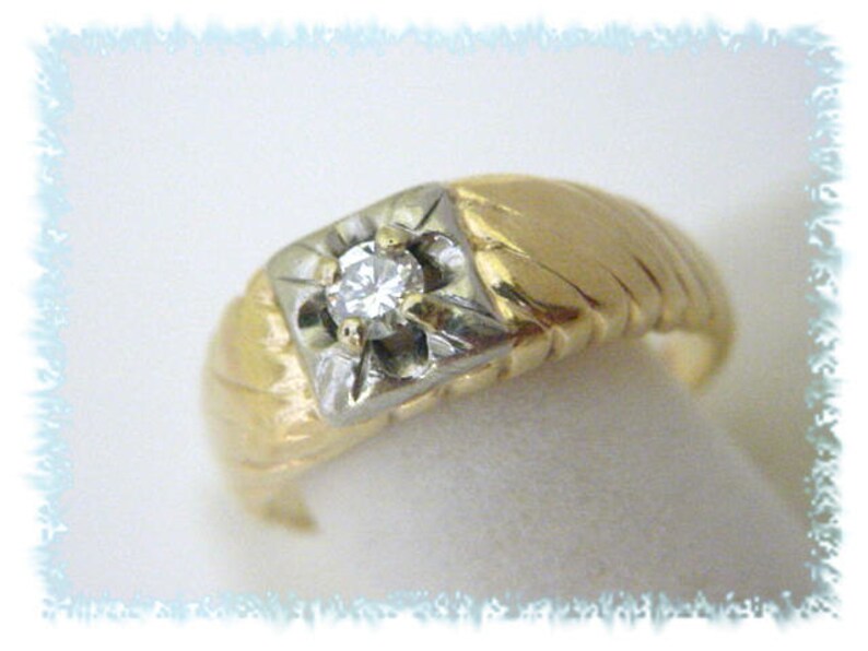 May include: A gold and white ring with a single diamond in the center. The ring has a textured band.