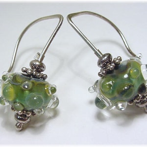 May include: A pair of silver dangle earrings with green and clear glass beads. The beads are irregular in shape and have a bubbly texture.