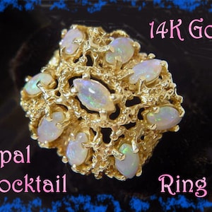 May include: A 14K gold cocktail ring featuring multiple oval opals. The ring has a textured, organic design, with the opals set within the gold. The ring is a statement piece, with the words "Opal Cocktail Ring" in pink.