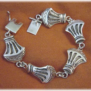 May include: A silver bracelet featuring five decorative, bell-shaped charms. Each charm has a detailed, geometric design.