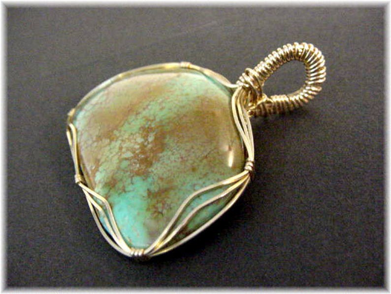 May include: A turquoise gemstone pendant with a gold wire wrap. The stone has a mottled green and brown pattern.