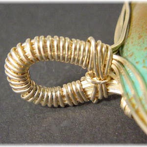 May include: Close-up of a gold wire wrapped around a turquoise stone pendant. The wire is wrapped in a tight coil, creating a decorative detail.