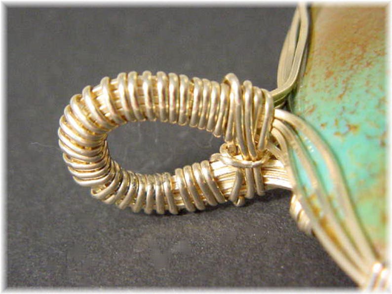 May include: Close-up of a gold wire wrapped around a turquoise stone pendant. The wire is wrapped in a tight coil, creating a decorative detail.