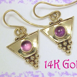 May include: Gold earrings with a geometric design. Each earring has a triangular shape with a round, pink gemstone and a cluster of small gold beads. The text "14K Gold" is visible. The earrings are made of gold.