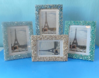 May include: Four rectangular picture frames with textured, crushed glass borders in shades of blue, teal, and silver. Each frame contains a photograph of the Eiffel Tower in Paris, displayed against a solid light blue background.