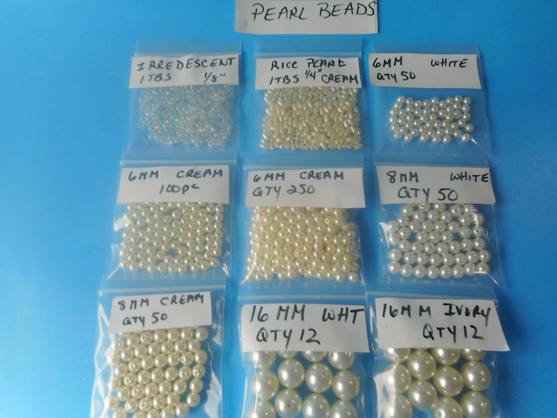 May include: Nine clear plastic bags containing various pearl beads, labeled with sizes and quantities. Labels include Iridescent 1/8 inch, Rice Pearl 1/4 inch, 6mm White, 6mm Cream 100pc, 6mm Cream 250, 8mm White, 8mm Cream 50, 16mm White, and 16mm Ivory.