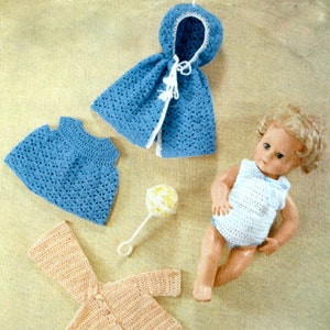 May include: A set of crocheted doll clothes, including a blue hooded jacket, a blue dress, a peach-coloured cardigan, and a white crocheted swimsuit. The doll clothes are laid out on a beige surface with a doll and a rattle.