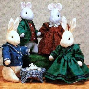 Könnte beinhalten: Vier Plüschkaninchen aus weißem Stoff, die verschiedene Outfits tragen. Die Kaninchen sitzen auf einer karierten Tischdecke mit einer Teekanne und Teetassen. Die Kaninchen tragen einen blauen Matrosenanzug, eine grüne Jacke, ein rotes Kleid und ein grünes Kleid.