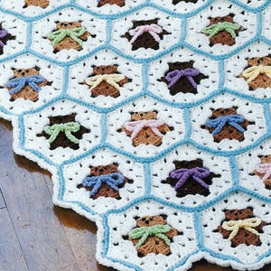 May include: A white crocheted baby blanket with a hexagonal pattern featuring brown teddy bears with colorful bows.