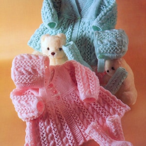 May include: A set of knitted baby clothes in pink and blue. The set includes a cardigan, a dress, a hat, and booties. The clothes are made with a cable knit pattern.