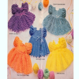 May include: Five crocheted baby dresses in different colours and patterns. The dresses are lavender, blue, light blue, orange, and yellow. The dresses are all made with different stitches and have different embellishments. The dresses are all laid out on a white background with balls of yarn.