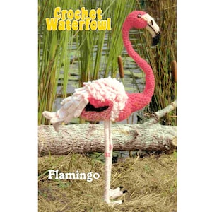 May include: A pink crocheted flamingo with a white ruffled neck, standing on a brown log with green reeds in the background. The text "Crochet Waterfowl" is in yellow letters at the top of the image and "Flamingo" is at the bottom.