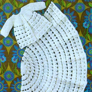 May include: White crocheted baby outfit with a jacket and a long skirt. The outfit is made with a delicate open stitch pattern.