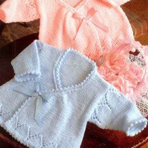 May include: Two knitted baby sweaters, one pink and one light blue, with delicate lace patterns and ribbon ties.