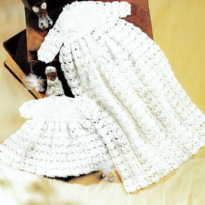 May include: Two white crocheted baby dresses, one larger than the other, laid out on a beige surface.