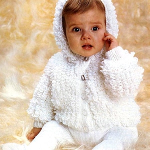 Puede incluir: Una chaqueta de punto blanca para bebé con capucha. La chaqueta tiene un aspecto texturizado y esponjoso y se abrocha en la parte delantera.