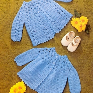 May include: Two light blue crocheted baby sweaters with button closures. The sweaters are laid out on a brown textured surface. The number "4" is visible in the top left corner of the image and the number "5" is visible in the bottom right corner of the image.
