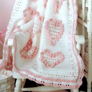 Puede incluir: Una manta de bebé de ganchillo blanco con un borde rosa y corazones de ganchillo rosa.