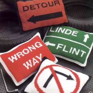 K&ouml;nnte beinhalten: Vier geh&auml;kelte Kissen in Form von Verkehrsschildern. Die Schilder zeigen "Umleitung", "Falsche Richtung", "Linde Flint" und ein Schild mit einem Rechtsabbiegeverbot.
