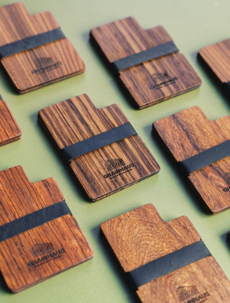 Puede incluir: Varias tarjetas de cartera de madera con una banda el&aacute;stica negra. Cada tarjeta tiene el texto "GRAINHAUS" y un logotipo de una ola estilizada.