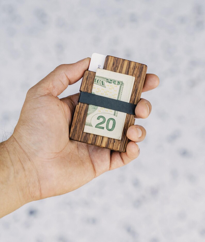 Puede incluir: Una cartera de madera con una banda el&aacute;stica negra que sostiene un billete de veinte euros y una tarjeta de cr&eacute;dito.