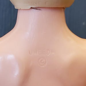 May include: Close-up of the back of a doll's head, showing a copyright symbol and the text "UN-ED-".