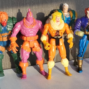 May include: Five action figures, including a purple and orange figure, a yellow and orange figure, a blue and green figure, a blue and purple figure, and a blue and white figure.