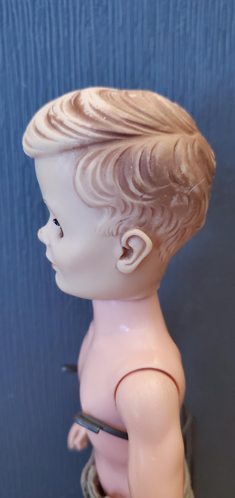 May include: A vintage plastic doll with a sculpted hairstyle and a light pink body. The doll is wearing a brown and white striped outfit.