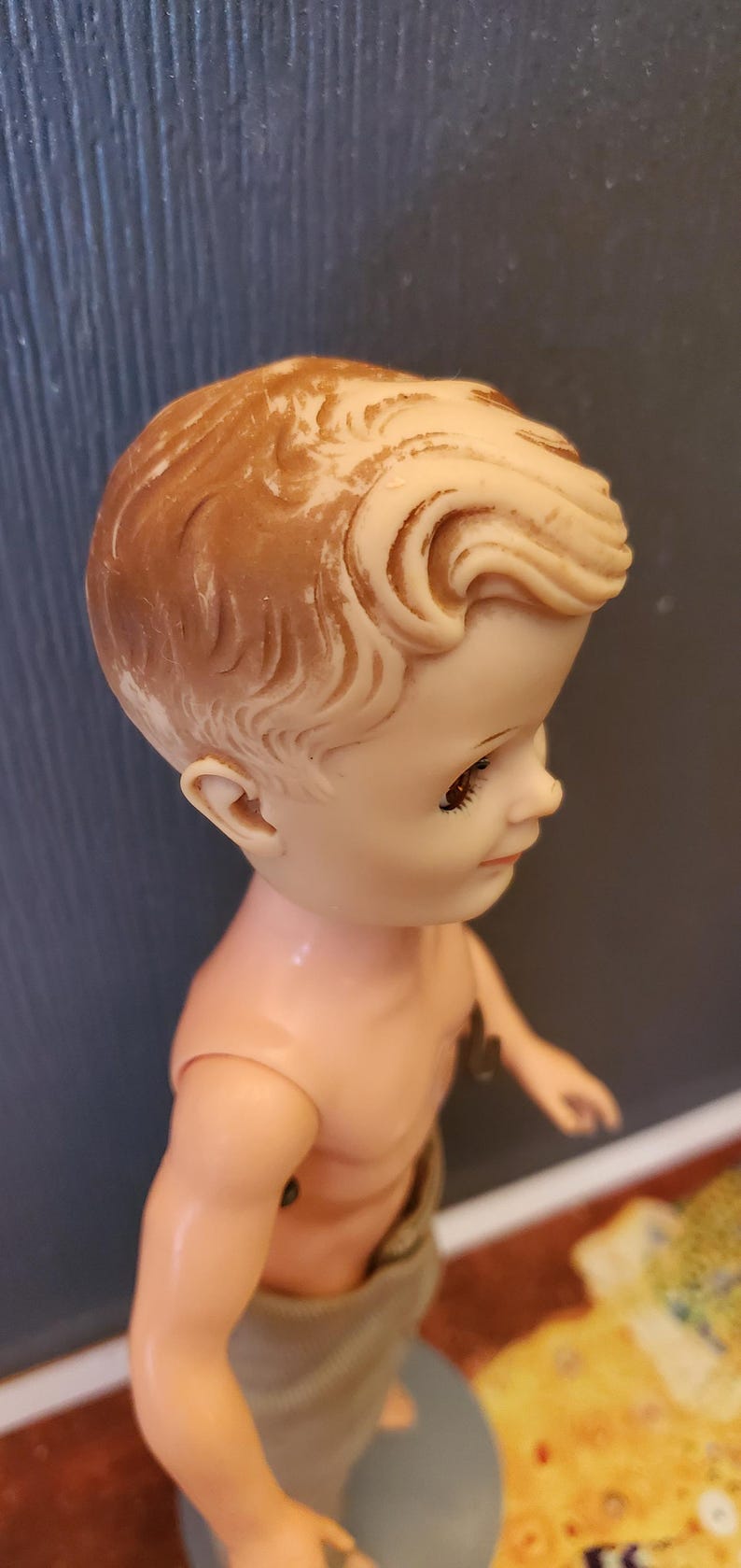 May include: A vintage plastic doll with a sculpted hairstyle and brown eyes. The doll is wearing a beige cloth towel around its waist.