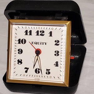 May include: A black and gold alarm clock with a white face and black numbers. The clock says "EQUITY" and "CHINA" on the face.