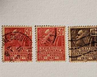 May include: Three vintage postage stamps from France, featuring a red, a brown, and a black stamp. Each stamp depicts a profile of a person's head and the text "Exposition Coloniale Internationale de Paris 1931". The stamps are in good condition and have a slight yellowing.