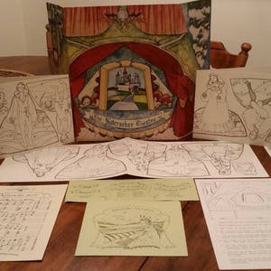 May include: A set of paper doll cutouts featuring a princess, a castle, and a stage. The paper dolls are black and white line drawings on white paper. The castle and stage are on a colorful background with a red curtain and a green stage.