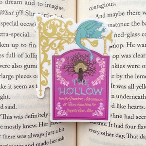 May include: A pink and white sign with a whimsical illustration of a house in a tree. The sign reads "The Hollow Inn for Travelers, Adventurers, & Those Searching for Happily Ever After". A blue dragon is perched on top of the sign.