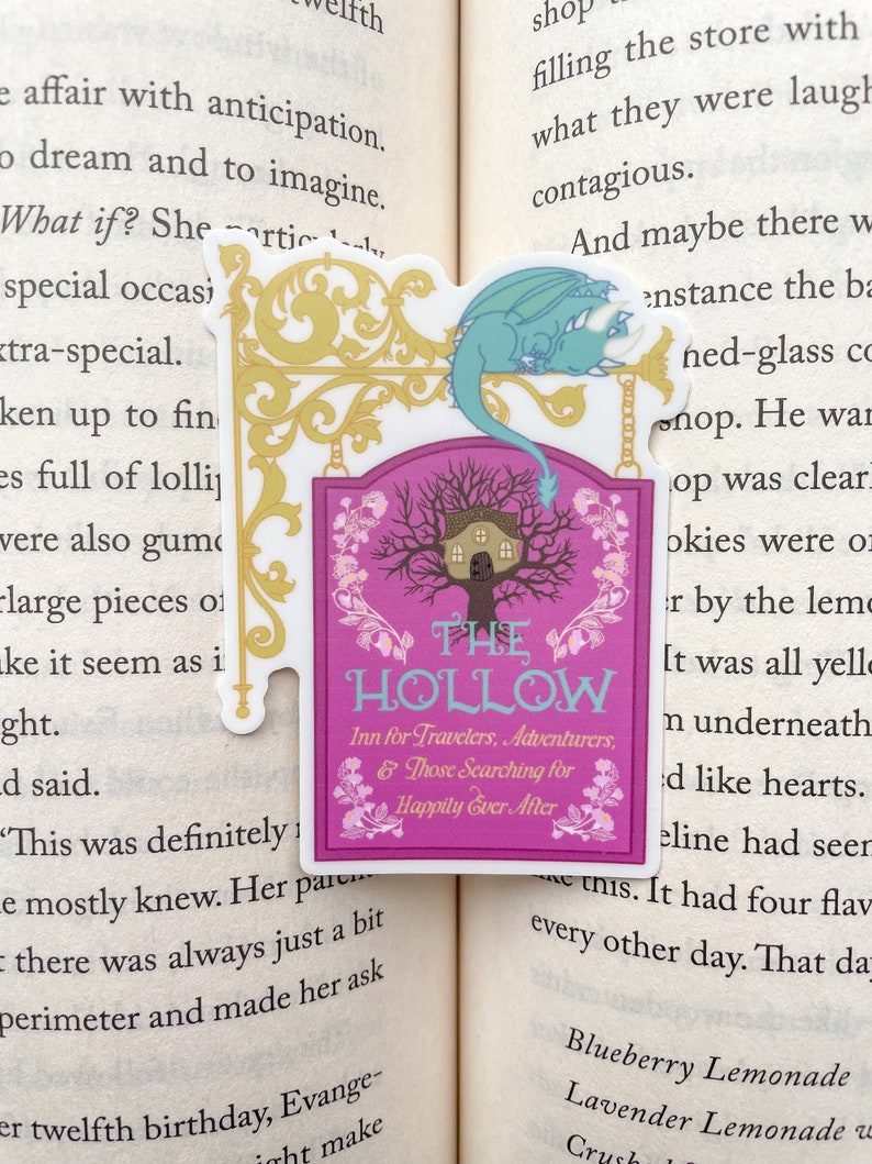 May include: A pink and white sign with a whimsical illustration of a house in a tree. The sign reads "The Hollow Inn for Travelers, Adventurers, & Those Searching for Happily Ever After". A blue dragon is perched on top of the sign.