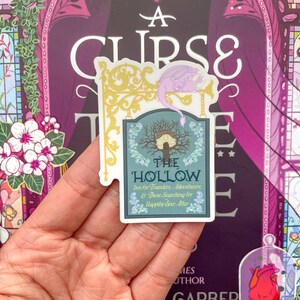 May include: A sticker featuring a whimsical illustration of a house in a tree with a dragon perched on a sign that reads "The Hollow Inn for Travelers, Adventurers, & Those Searching for Happily Ever After."