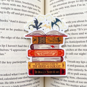 May include: A sticker featuring a stack of fantasy books with dragon riders on the cover. The books are titled "Fables of the Barren", "Colonel Kaori's Field Guide to Dragonkind", "Major Afrenda's Guide to the Riders Quadrant", and "The Dragon Riders Codex".
