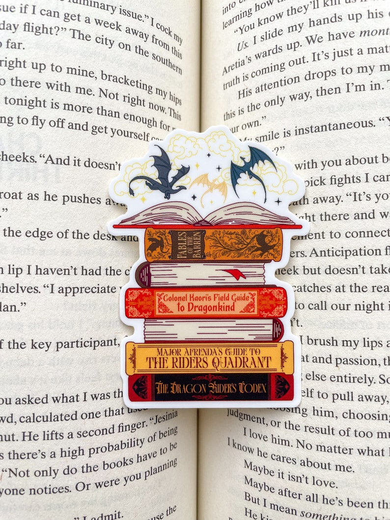 May include: A sticker featuring a stack of fantasy books with dragon riders on the cover. The books are titled "Fables of the Barren", "Colonel Kaori's Field Guide to Dragonkind", "Major Afrenda's Guide to the Riders Quadrant", and "The Dragon Riders Codex".