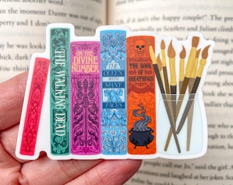 May include: A sticker featuring a stack of five colorful books with titles like "The Walking Dead", "On the Divine Number", "The Queen with Many Faces", "The Book of Breathings", and a cauldron with smoke coming out of it. There are also five paintbrushes in a glass jar.