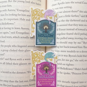 May include: A pink and gold sign with a whimsical font reads "The Hollow Inn for Travelers, Adventurers, & Those Searching for Happily Ever After". A light blue dragon with gold accents is perched on the sign.