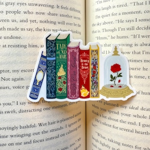 Può includere: Un foglio di adesivi con disegni a tema libri. Presenta una pila di libri colorati con titoli come "Tale as Old as Time" e "Beauty & the Beast". Include anche una cupola di vetro con una rosa rossa.