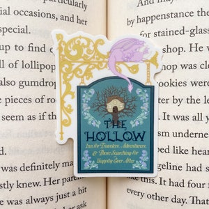 May include: A sticker featuring a sign for "The Hollow Inn for Travelers, Adventurers, & Those Searching for Happily Ever After". The sign is decorated with a whimsical tree and a small house. A purple dragon sticker is placed above the sign.